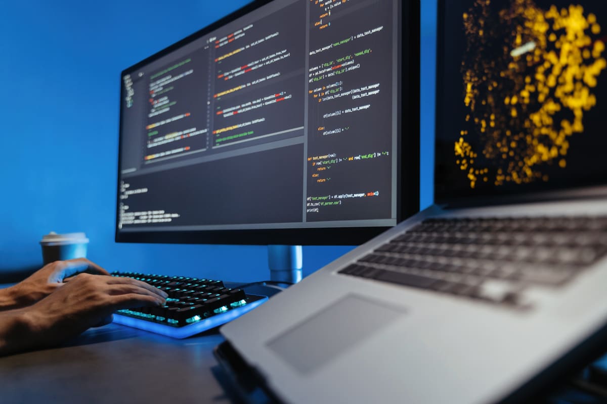 Developer writing website code on a computer with a glowing keyboard at night